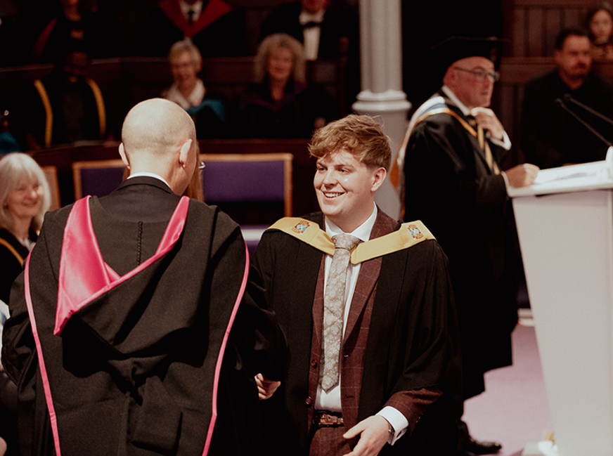 male graduate on stage shaking hands with principal