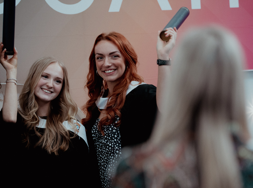 two female students smiling at camera holding scrolls 