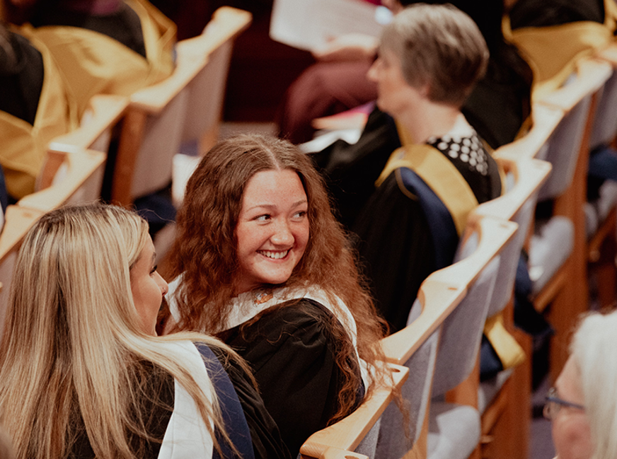 graduate turned in her chair smiling at graduate behind her 
