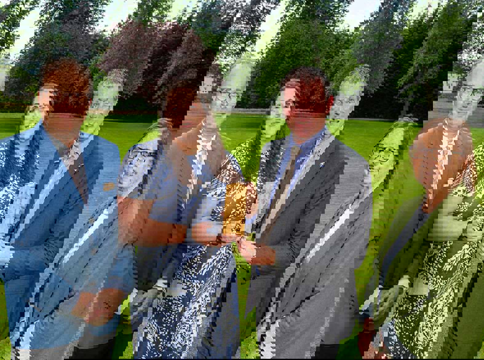 Four people standing on grass holding a wooden award