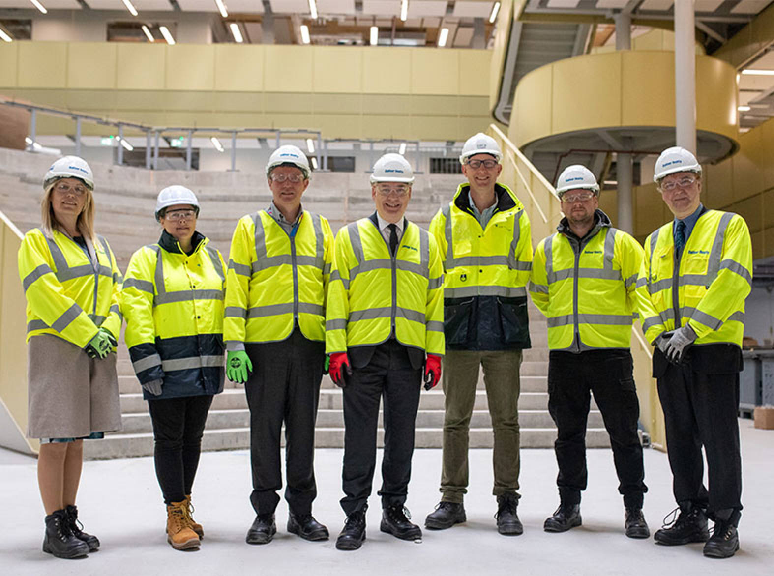 A group of people wearing personal proective equipment standing in a builing 