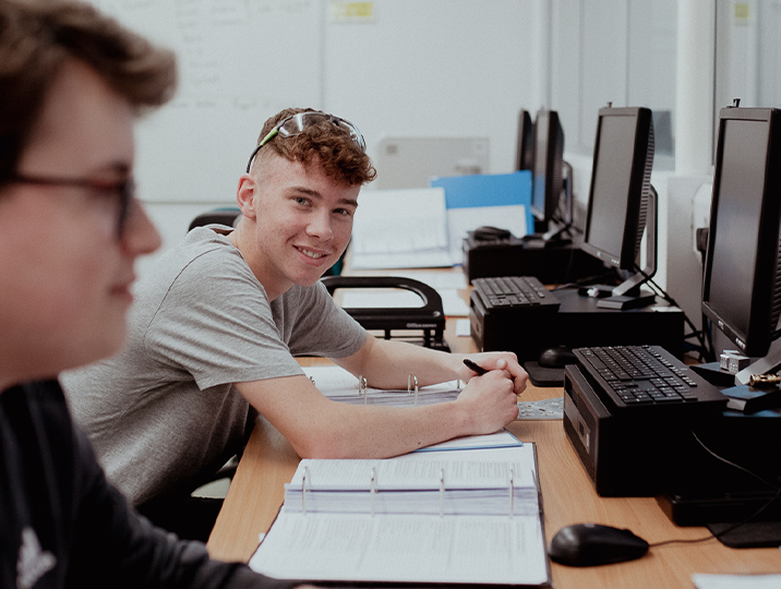 male student sitting in front of computer smiling at camera 