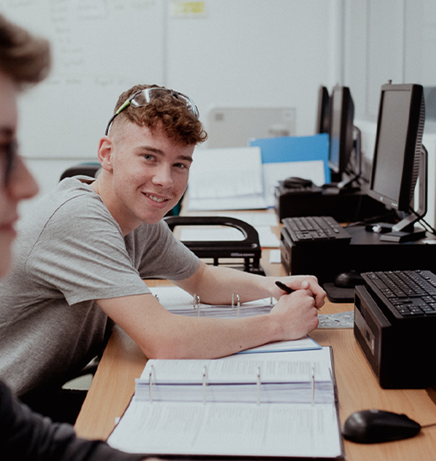 male student sitting in front of computer smiling at camera male student sitting in front of computer smiling at camera