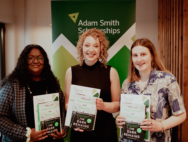 three scholarship winners holding certificate smiling at camera with adam smith banner in background
