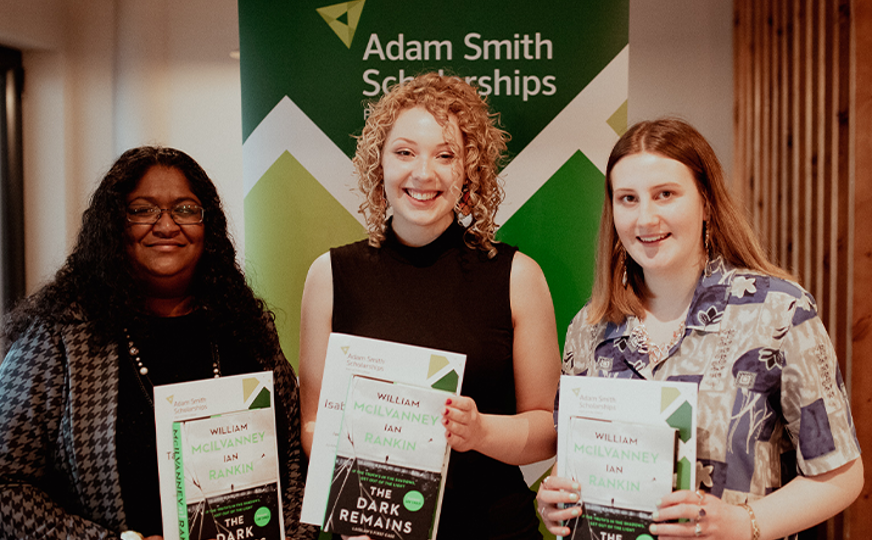 three scholarship winners holding certificate smiling at camera with adam smith banner in background